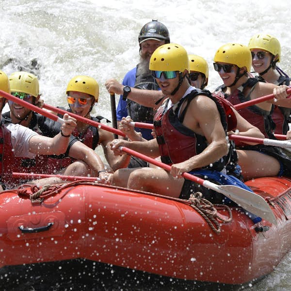 Group of people wearing life vests and helmets raft down a turbulent river in an inflatable boat, paddles engaged. Group of people wearing life vests and helmets raft down a turbulent river in an inflatable boat, paddles engaged.