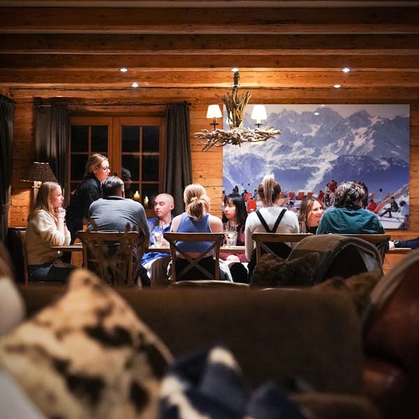 A group of people sitting around a table in a cozy wooden cabin, with a large mountain landscape painting on the wall behind them. A group of people sitting around a table in a cozy wooden cabin, with a large mountain landscape painting on the wall behind them.