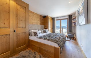accommodation - Apartment Basalte - A cozy bedroom with a wooden interior features a neatly made double bed with white linens and a brown fur blanket. A door opens to a bathroom, and a hallway leads to another space.