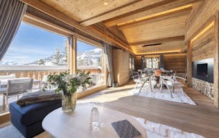 accommodation - Chalet Daphne - Spacious wooden chalet interior with large windows, dining area, and seating. Views of mountains and trees outside. Modern decor with natural tones and cozy ambiance.