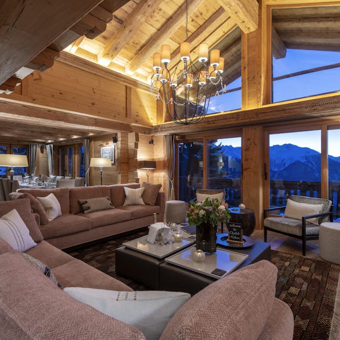 accommodation - Chalet Milou - cosy chalet living room with sofas and chairs in front of a roaring fire, under a decorative chandelier.