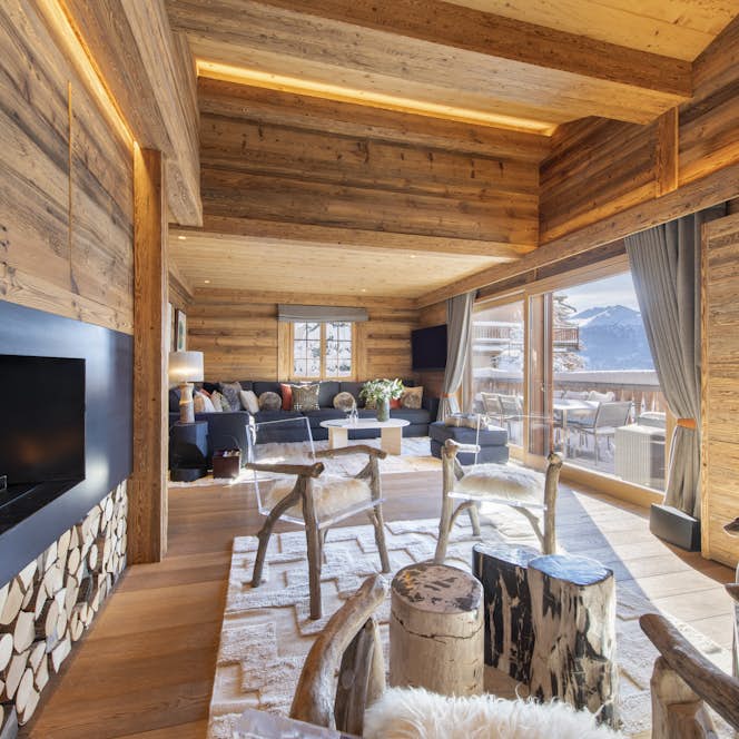 accommodation - Chalet Daphne - Cozy wooden living room with a modern fireplace, rustic chairs, and couches. Large glass doors open to a mountain view balcony.