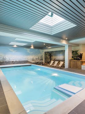 accommodation - Apartment Hickory - Indoor swimming pool with lounge chairs and mountain-themed wall murals. Ceiling lights and a skylight illuminate the area.