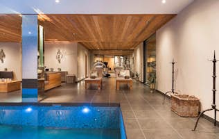 accommodation - The Alpine Estate - Luxurious indoor pool area with stone wall, wooden ceiling, lounge chairs, and modern decor.