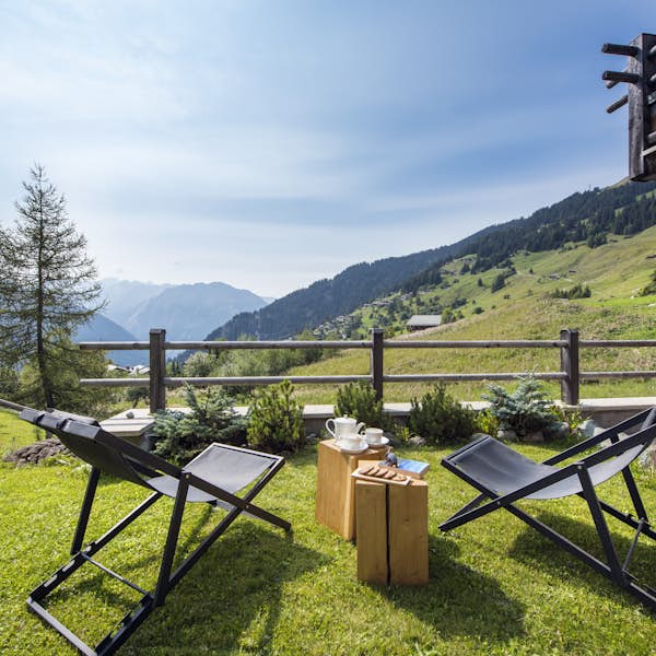 Two lounge chairs in a grassy outdoor space overlooking mountain views. Two lounge chairs in a grassy outdoor space overlooking mountain views.