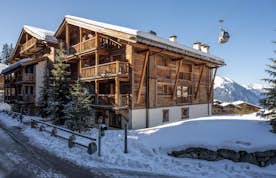 accommodation - Apartment Basalte - Wooden chalet in a snowy mountain setting with a gondola lift in the background, under a clear blue sky.